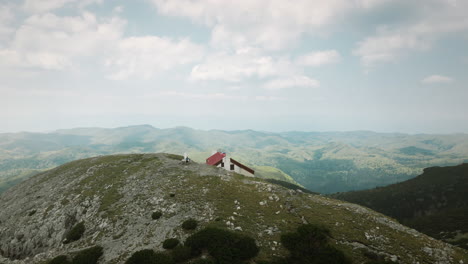 a drone shot of a peak of mountain snežnik with a mountain cottage, with a mid range visibility of near mountains