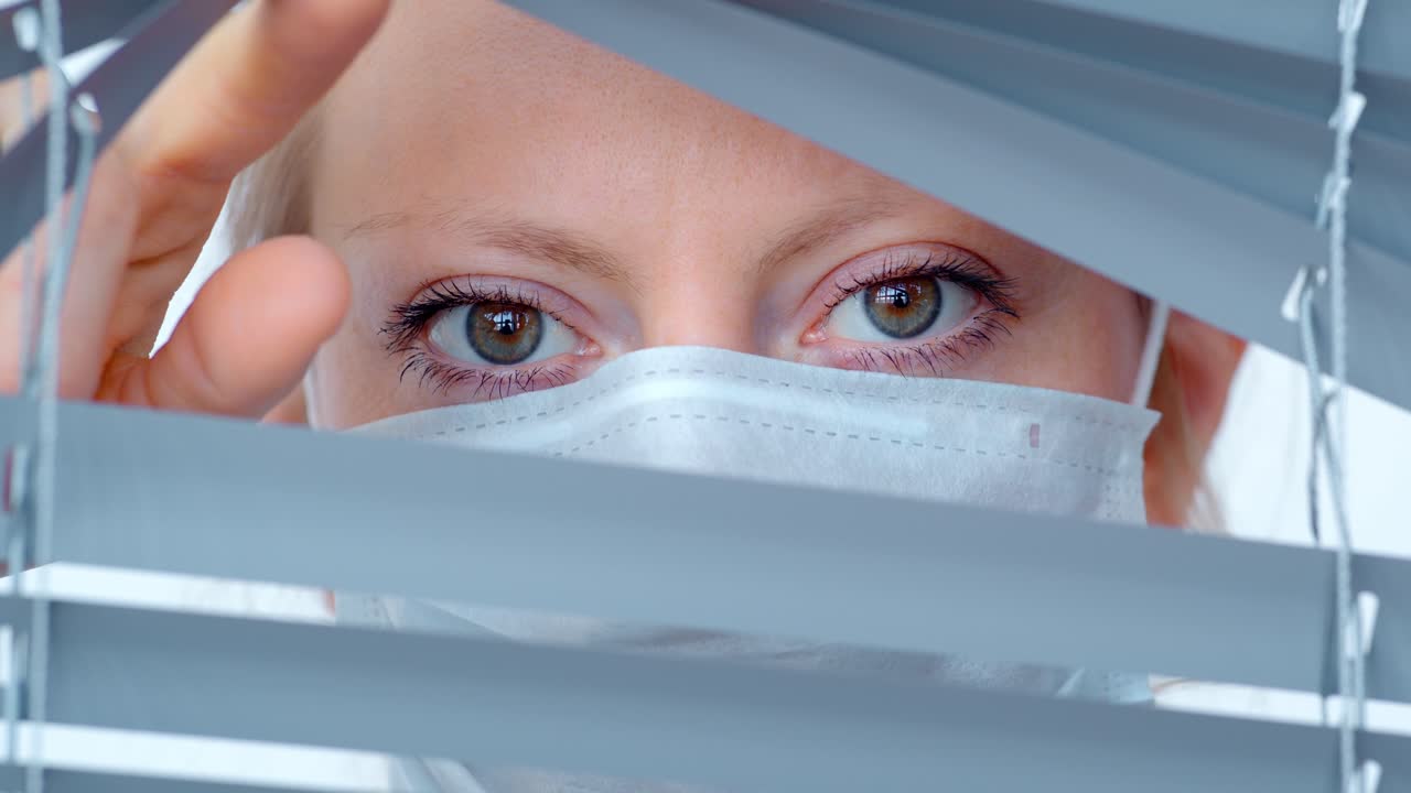 Donna con mascherina che guarda attraverso le persiane