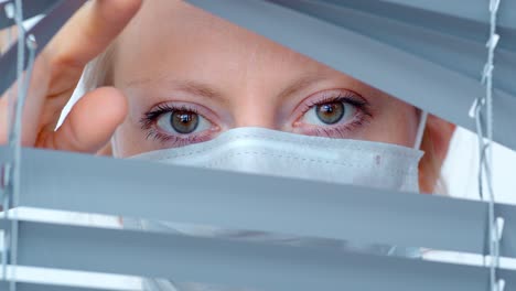woman wearing mask looking through blinds