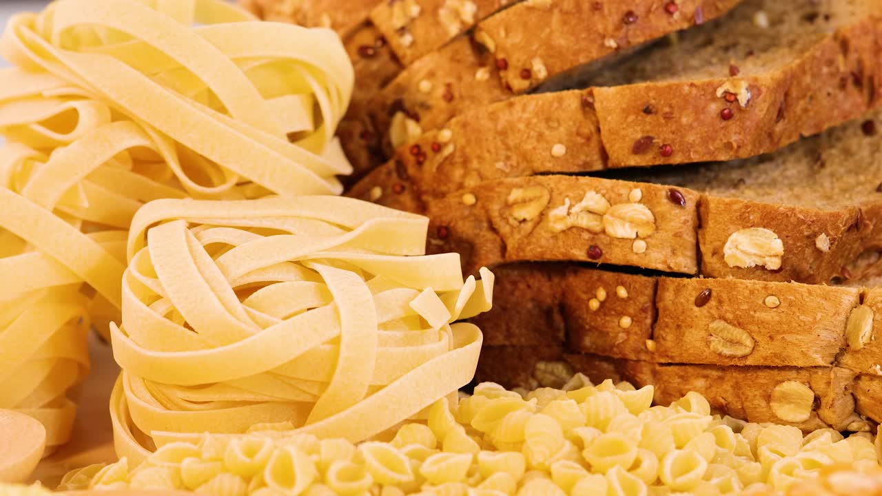 Close-up of various grains, pasta, and sliced whole wheat bread under warm lighting, showcasing texture and detail