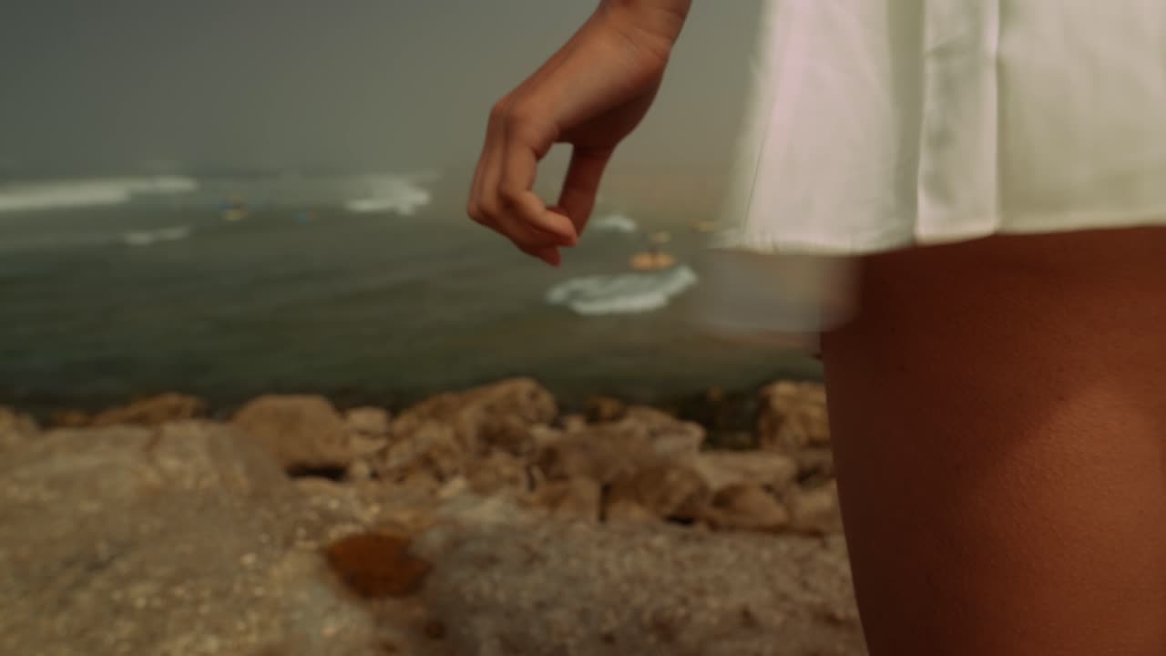 Woman Standing on Rocky Shore with Hand on White Dress