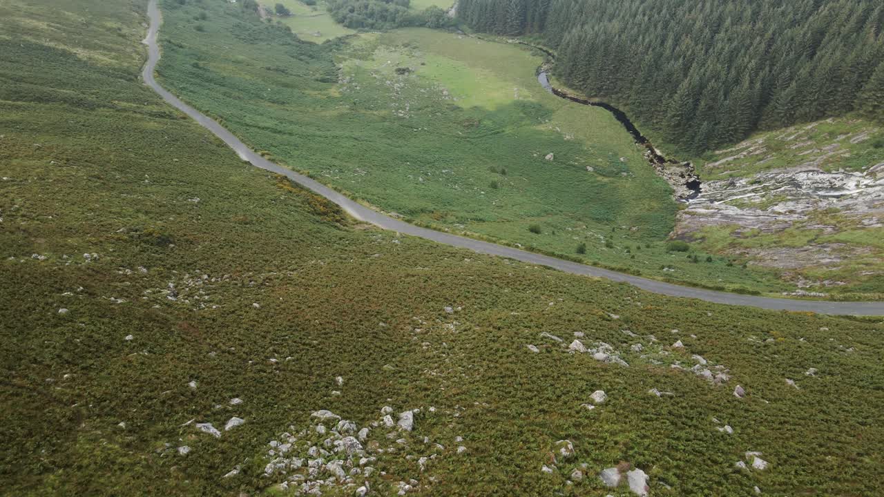 camino estrecho a lo largo del valle verde en las montañas wicklow en irlanda con una cascada que fluye hacia el arroyo en una mañana temprana - dron aéreo