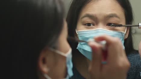 girl with face mask applying mascara facing mirror, slow motion