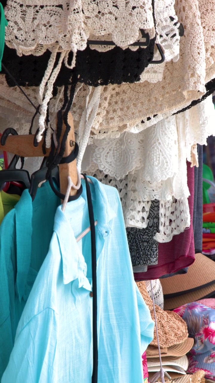 Primo piano di camicie azzurre e costumi da bagno in pizzo appesi in un mercato tropicale all'aperto.