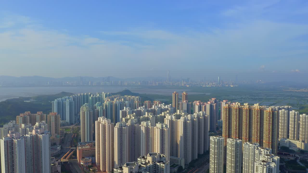toma cinematográfica de un dron que viaja hacia atrás sobre un suburbio de hong kong durante el día, la ciudad distante shenzen es visible