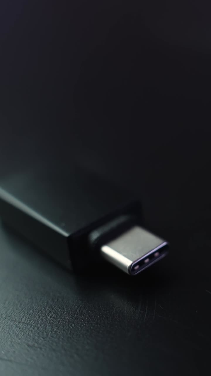 Moody macro shot of a USB-C connector on a dark desk surface with soft blur and plenty of copy space, minimal tech vibe in a vertical frame