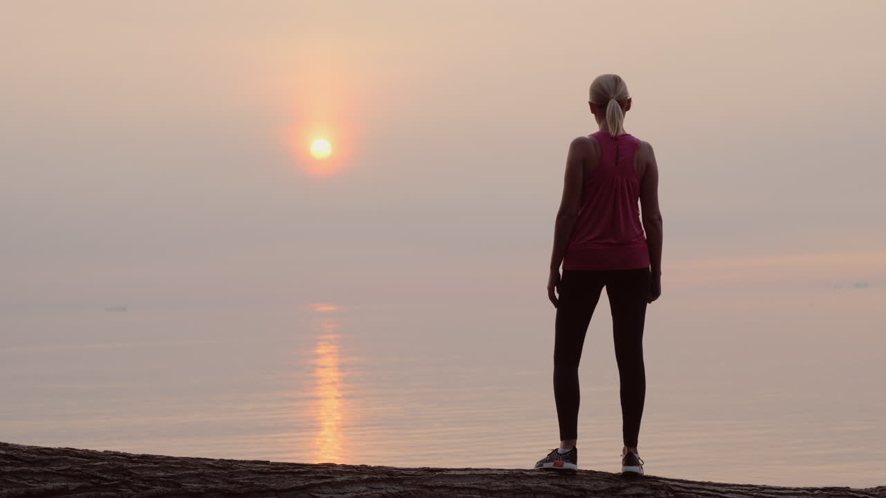 바다 뒷모습 너머로 새벽을 바라보는 자신감 있는 피트니스 여성