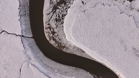 aerial top-down view of a winding river through snowy terrain near borgarfjörður, iceland, with striking natural contrast.