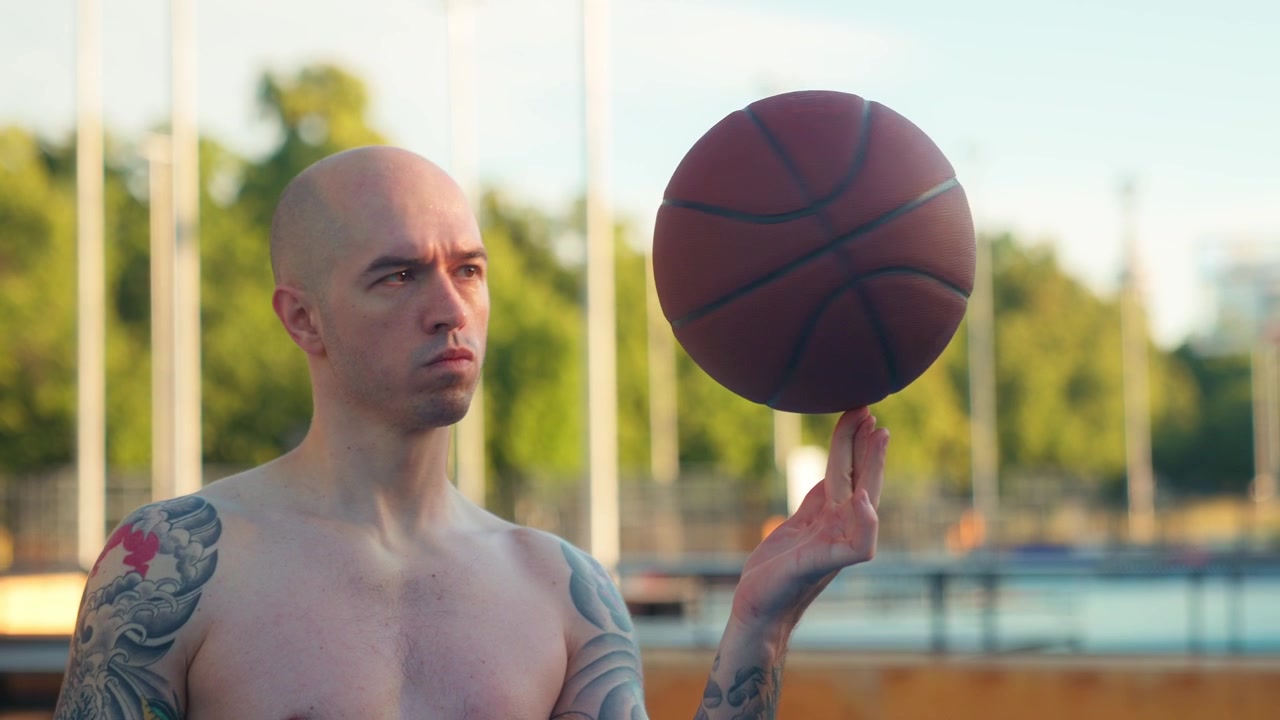 Homem careca com tatuagens girando bola de basquete no dedo ao ar livre