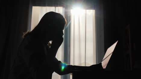 silhouette of woman communicating through the headset while using a laptop