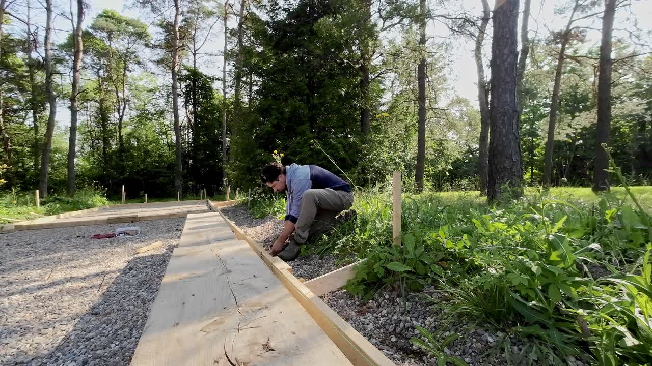 Residential Carpenter Screwing Wood Together On A Concrete Form Project Outdoors.