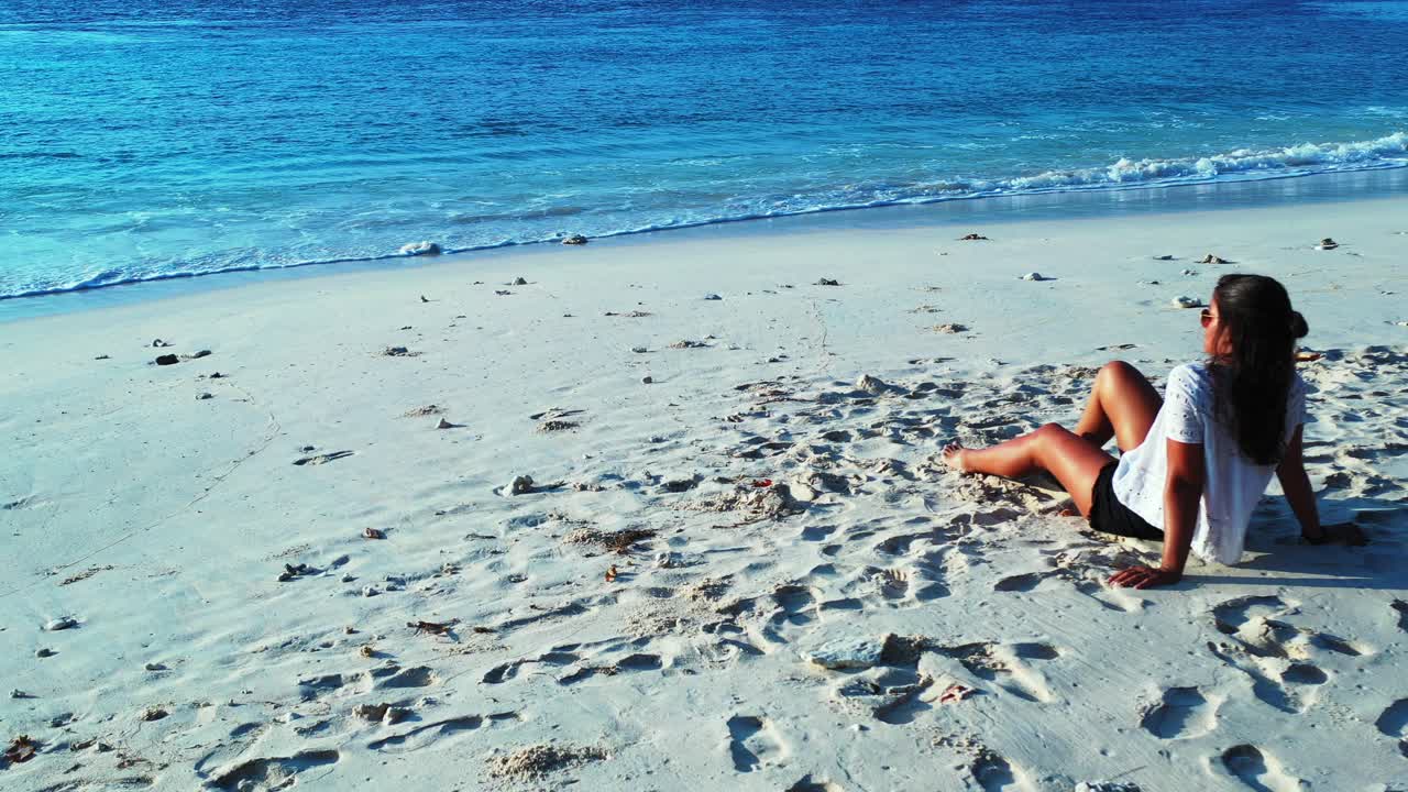 Girl sitting on white sandy beach in front of calm blue sea, meditating on quiet exotic seascape of tropical island in Dominican Republic