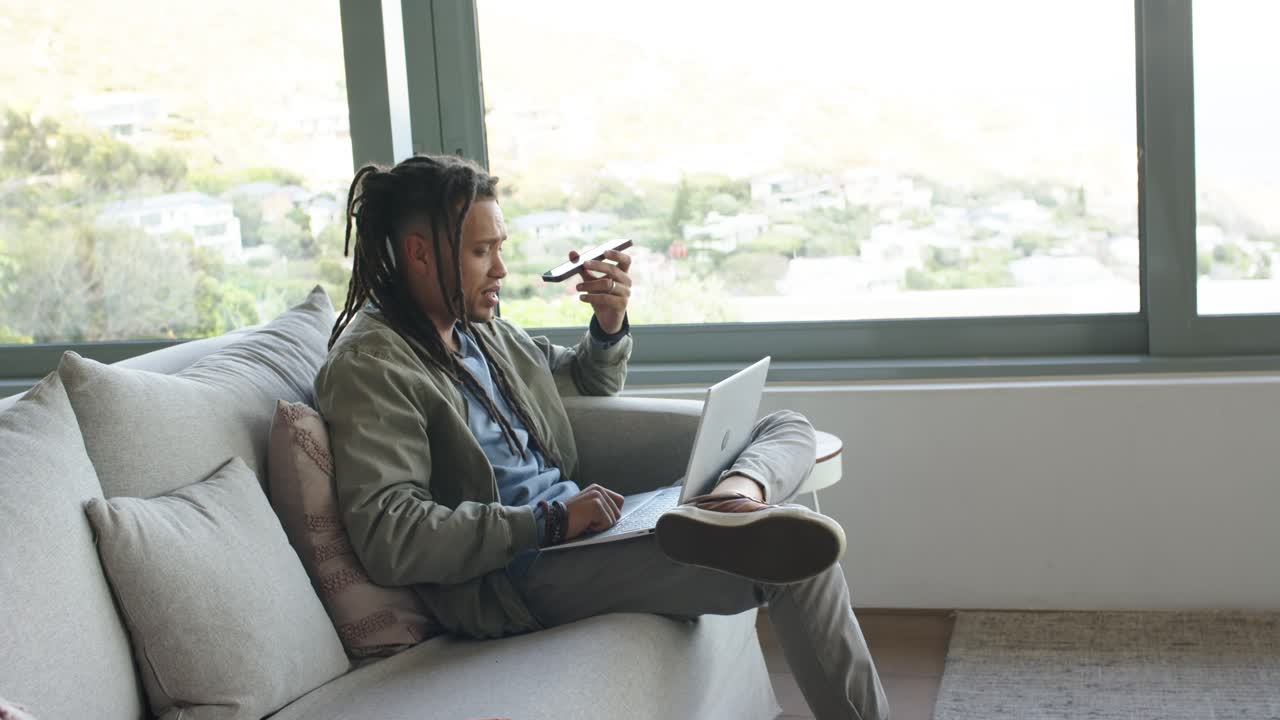 After checking laptop screen, man is grabbing smartphone and typing, speaking on call near window