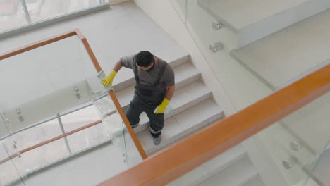 top view of arabic cleaning man wearing gloves cleaning stair railing and crystals inside an office building