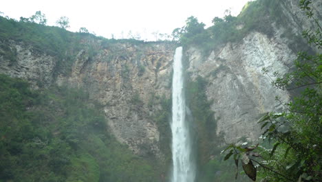 Panning-up-from-the-bottom-of-the-gorge-to-reveal-a-small-bridge-and-the-giant-Sipso-Piso-waterfall-in-North-Sumatra,-Indonesia