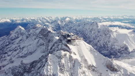 approaching aerial of the summit of zugspitze in winter with snow clouds and blue sky