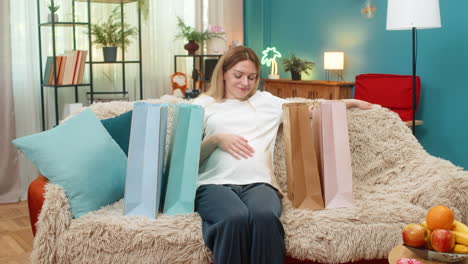 pregnant woman returns with shopping bags sets big load down smiles satisfied after baby store trip