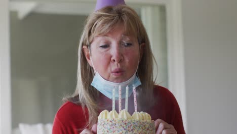 senior caucasian woman spending time at home, sitting in her living room blowing candles on birthday