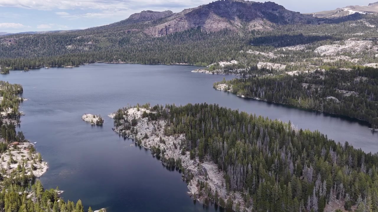 Riprese aeree con drone che sorvolano Silver Lake, rivelando le sue acque di un blu profondo circondate da una vasta pineta e montagne di granito nella catena della Sierra Nevada vicino a Pioneer, California.