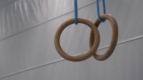 close-up of wooden gymnastic rings with blue ropes hanging and swaying