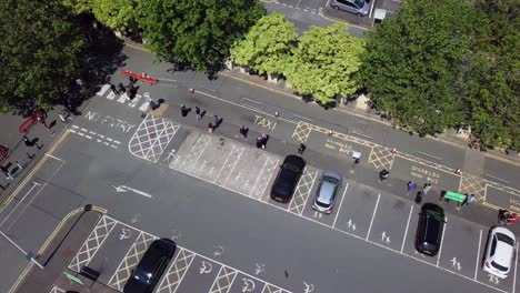 aerial drone view of people waiting in the line of a supermarket queue under sunshine during day while they keep their social distance and obey the hygiene rules as shopping