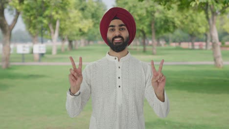 happy sikh indian man showing victory sign in park