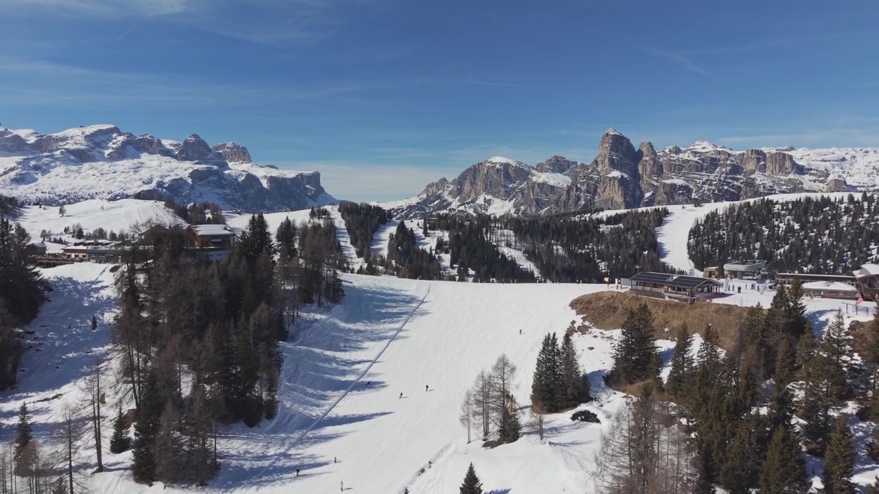 Ampia vista invernale dal Piz Sorega in Alta Badia, con sciatori che scendono pendii innevati sotto il Sassongher e il Gruppo del Sella sotto un cielo azzurro limpido