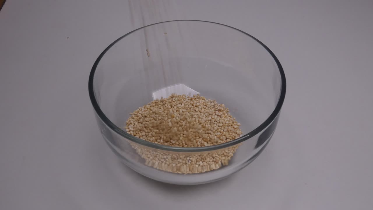 Peruvian raw white Quinoa being poured into a clear small glass bowl on a white background