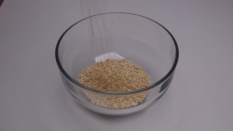 peruvian raw white quinoa being poured into a clear small glass bowl on a white background