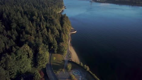 seawall and lush green coniferous trees at stanley park with lions gate bridge over the burrard inlet in vancouver, bc, canada