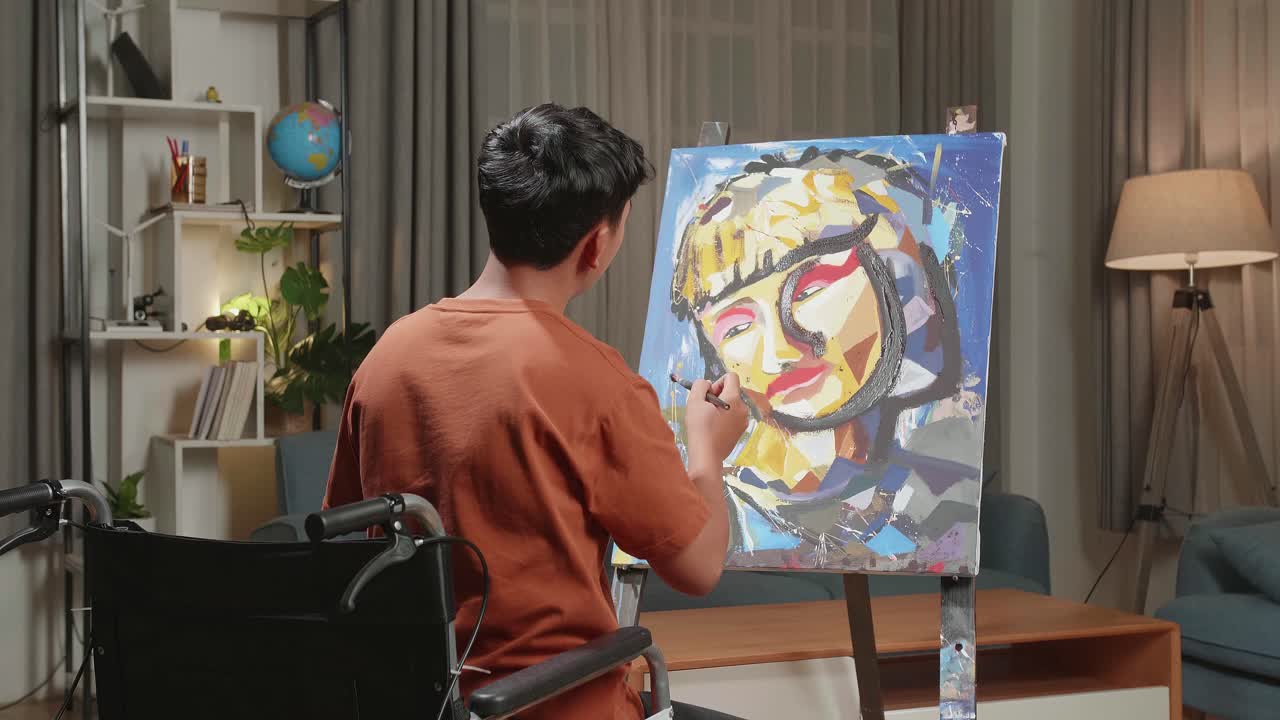 Hind View Of An Asian Artist Boy In Wheelchair Thinking And Painting A Girl'S Face On The Canvas