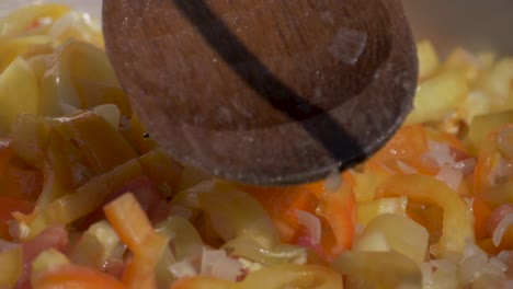 revolviendo un montón de tomates y pimientos en un caldero con una cuchara de madera durante la preparación de la cocina letcho - cámara lenta de 180 fps