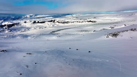 Luftaufnahme-Der-Landschaft-über-Menschen,-Die-Mit-Schneemobilen-Auf-Dem-Myrdalsjökull-Gletscher-In-Island-Fahren,-In-Der-Abenddämmerung