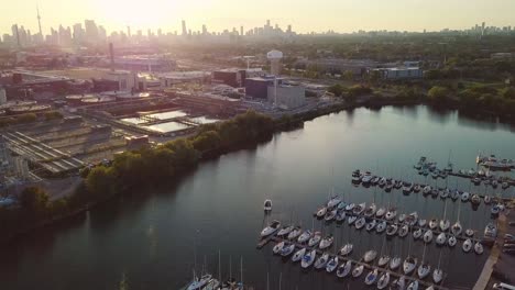 aerial sunset wide shot rising over lake ontario sailboat yacht marina dock with industrial factory and downtown skyline in background in toronto ontario canada