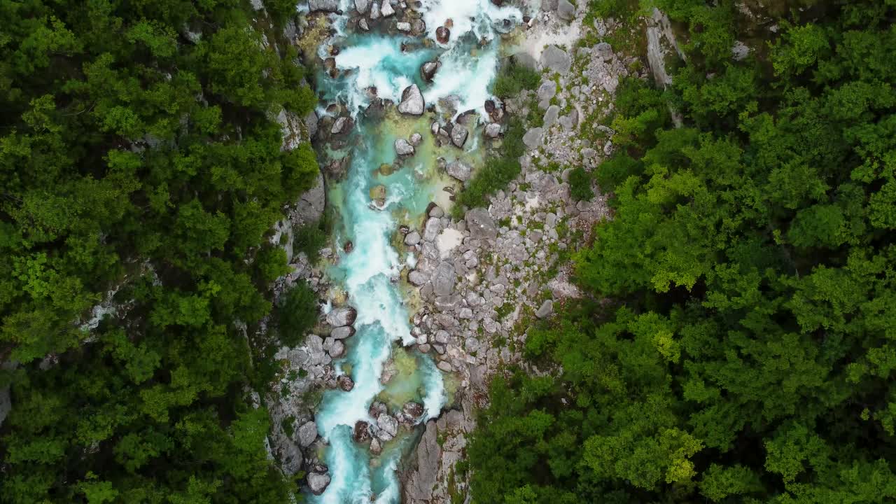 Aerial top down shot of flowing water in rocky stream surrounded by green forest trees - Boka Waterfall in Posočje Slovenia