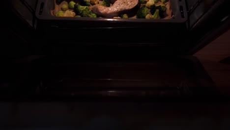 footage of delicious raw salon cutlets in a baking tray along with some vegetables , cooking in an oven