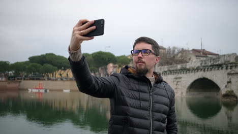 hombre tomando una selfie junto al río y el puente