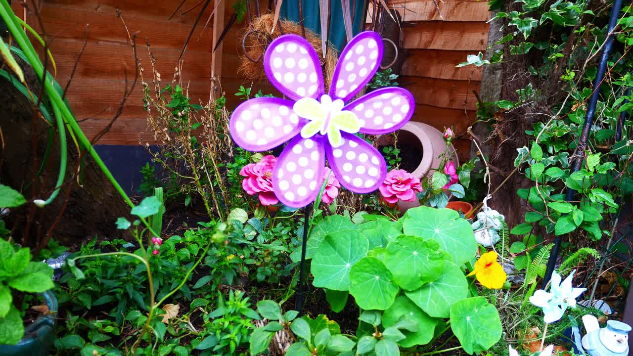 colorido molino de viento de mariposa giratorio infantil soplando en la brisa entre una variedad de flores y plantas en flor