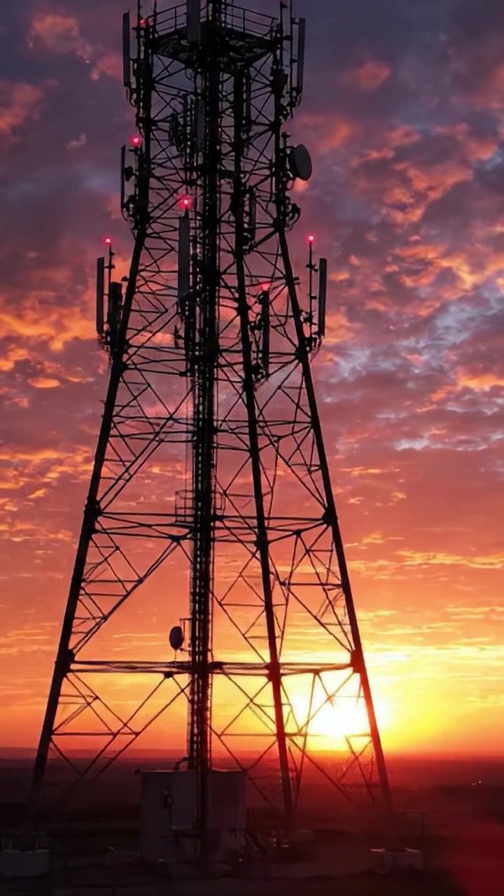 Un impresionante atardecer ilumina una torre de comunicaciones, proyectando siluetas contra un cielo vibrante de tonos naranjas y rosados, simbolizando conectividad y tecnología.