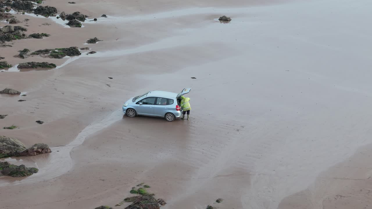Aerial view looking down at man loading sack into car on Sleeping bay beach cove before morning tide