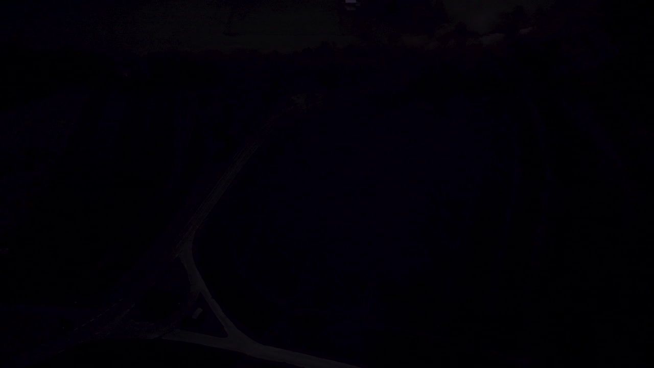 Drone tilts up revealing breathtaking early morning scene: an orange-glowing sunrise, a small town shrouded in low-hanging clouds, and birds flying by