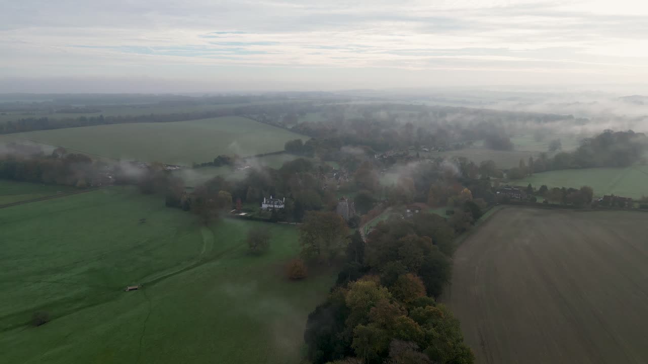 안개 속의 작은 마을을 향해 가을 색의 나무 줄을 넘어 비행