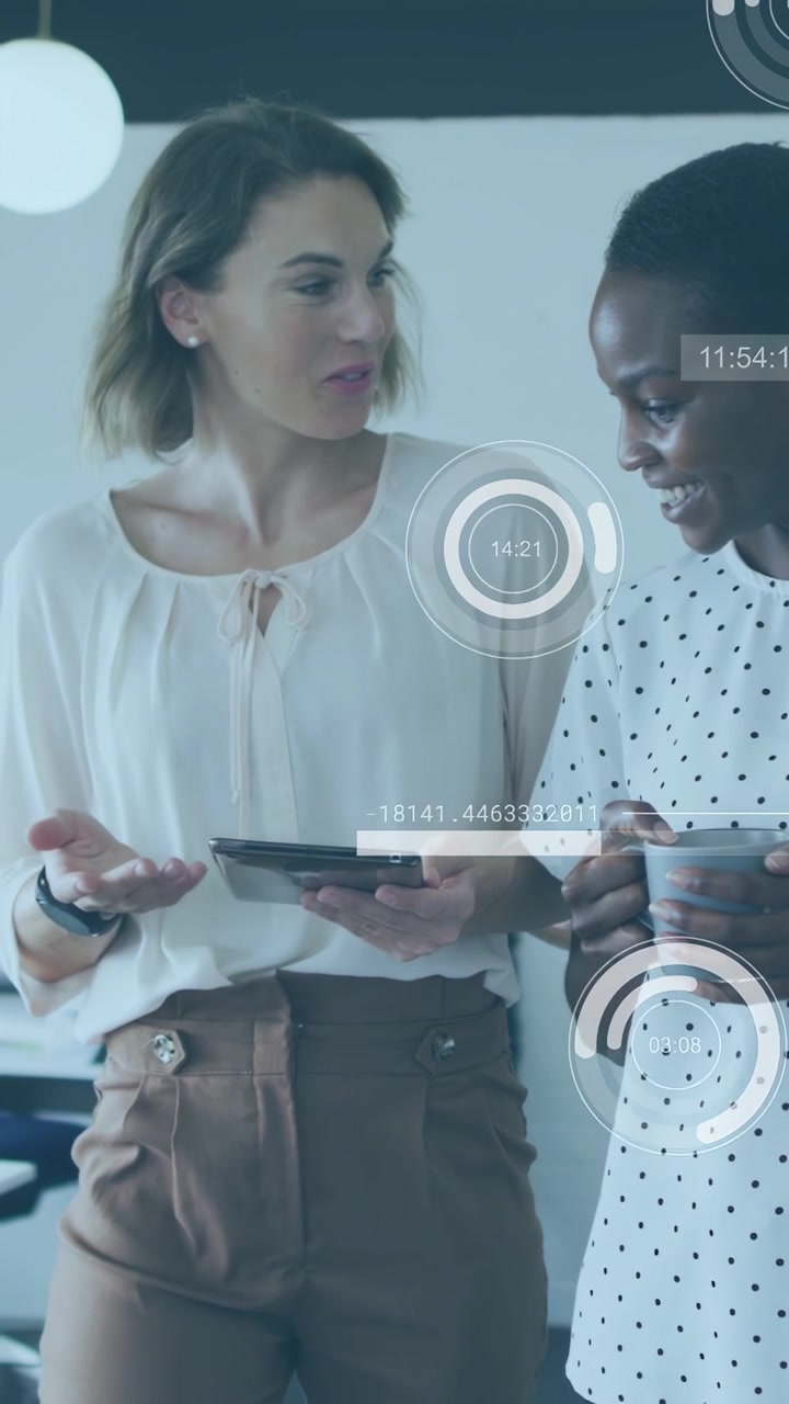 Vertical video: Peers in office, left woman tapping tablet starting data overlays reviewing metrics