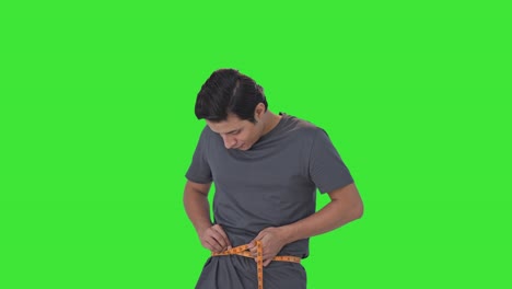 happy indian man measuring waist using inch tape green screen