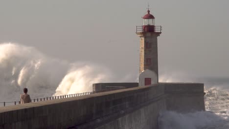 Grandes-Olas-Del-Océano-Chocan-Contra-El-Faro-Con-Una-Persona-En-Primer-Plano