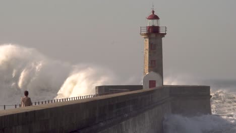 grandes olas del océano chocan contra el faro con una persona en primer plano