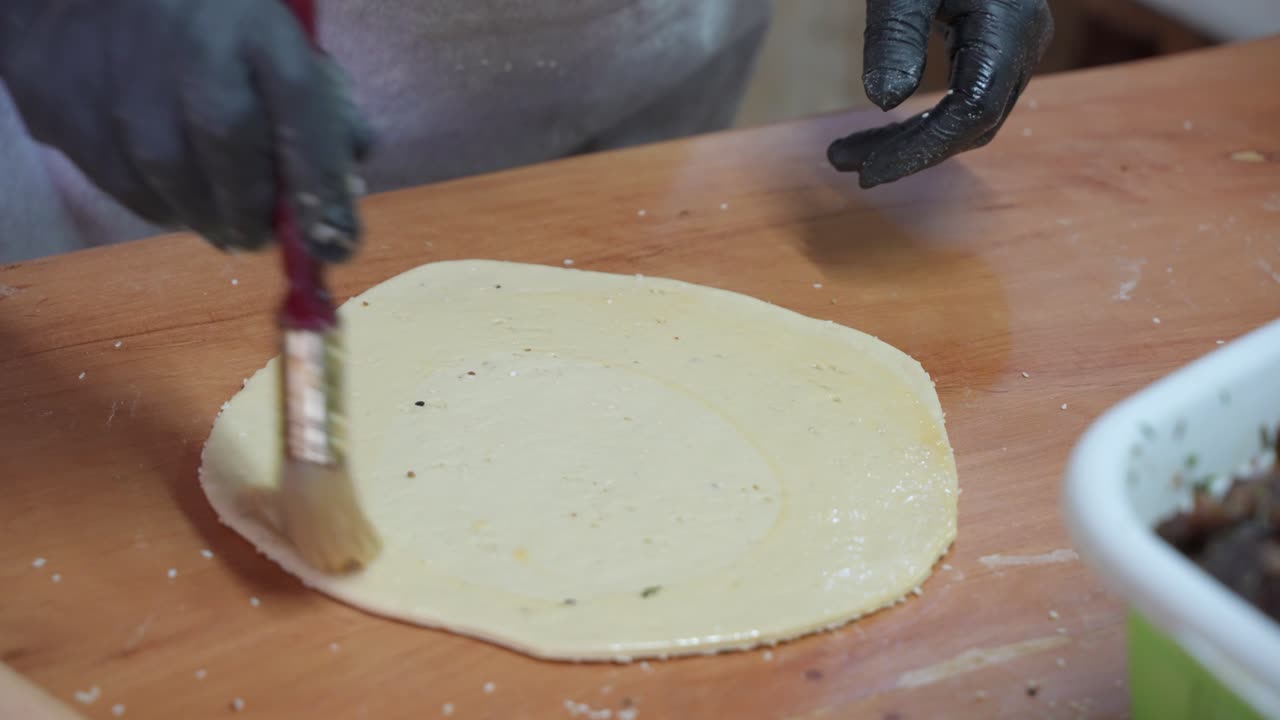primer plano de cepillado de masa de pastelería cruda aplanada con mantequilla, haciendo flaouna
