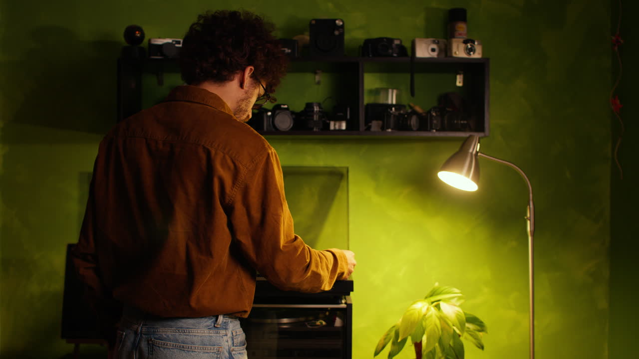 Giovane creativo che ascolta un disco in vinile in un accogliente studio domestico con macchine fotografiche vintage e illuminazione calda