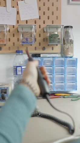 close-up of a person working on a craft project, possibly making jewelry, in an organized workshop