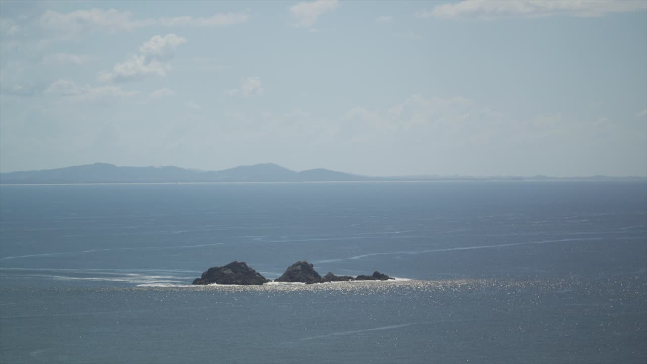 水面の動きが見える海に囲まれたジュリアンロックスのクローズアップ、地平線には遠くの地形、オーストラリア、バイロンベイ。